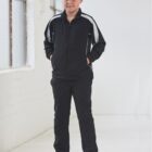 A boy in a black tracksuit stands with hands in pockets in a bright, white room.