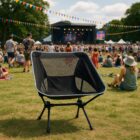 Black camping chair on grass at an outdoor music festival with a stage and crowd in background.
