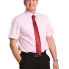 Man in short-sleeve pink shirt, red tie, and black pants smiling at the camera.