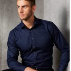 Man in a navy blue dress shirt sitting against a gray textured wall, looking to the side.