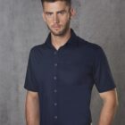 Man wearing a short-sleeve navy button-up shirt standing against a gray textured background.