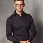 Man wearing glasses and a dark striped dress shirt, standing against a gray wall.