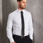 Man in striped dress shirt, black tie, and slacks standing against a gray concrete wall.