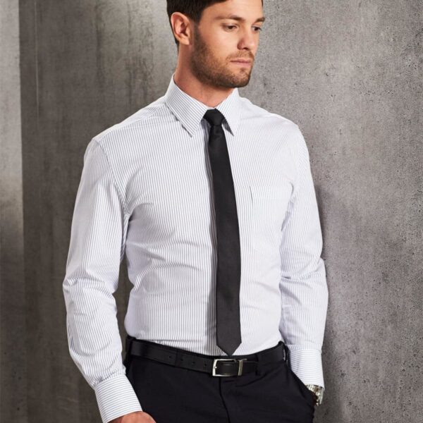Man in a striped dress shirt and tie standing against a gray wall, holding a briefcase.