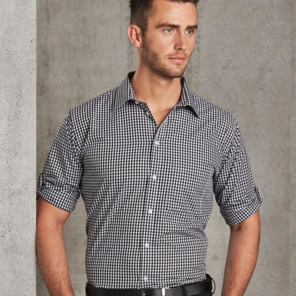 Man in a black and white checkered shirt standing against a gray concrete wall, looking sideways.