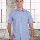 Smiling man in a blue checkered short-sleeve shirt standing in front of large windows.