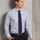 Man wearing a striped dress shirt, black tie, and black pants standing against a concrete wall.