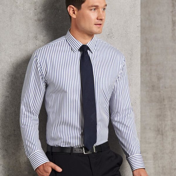 Man in striped dress shirt, black tie, and trousers stands by a gray textured wall.