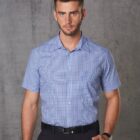 Man in a blue checked short-sleeve shirt standing against a gray textured background.