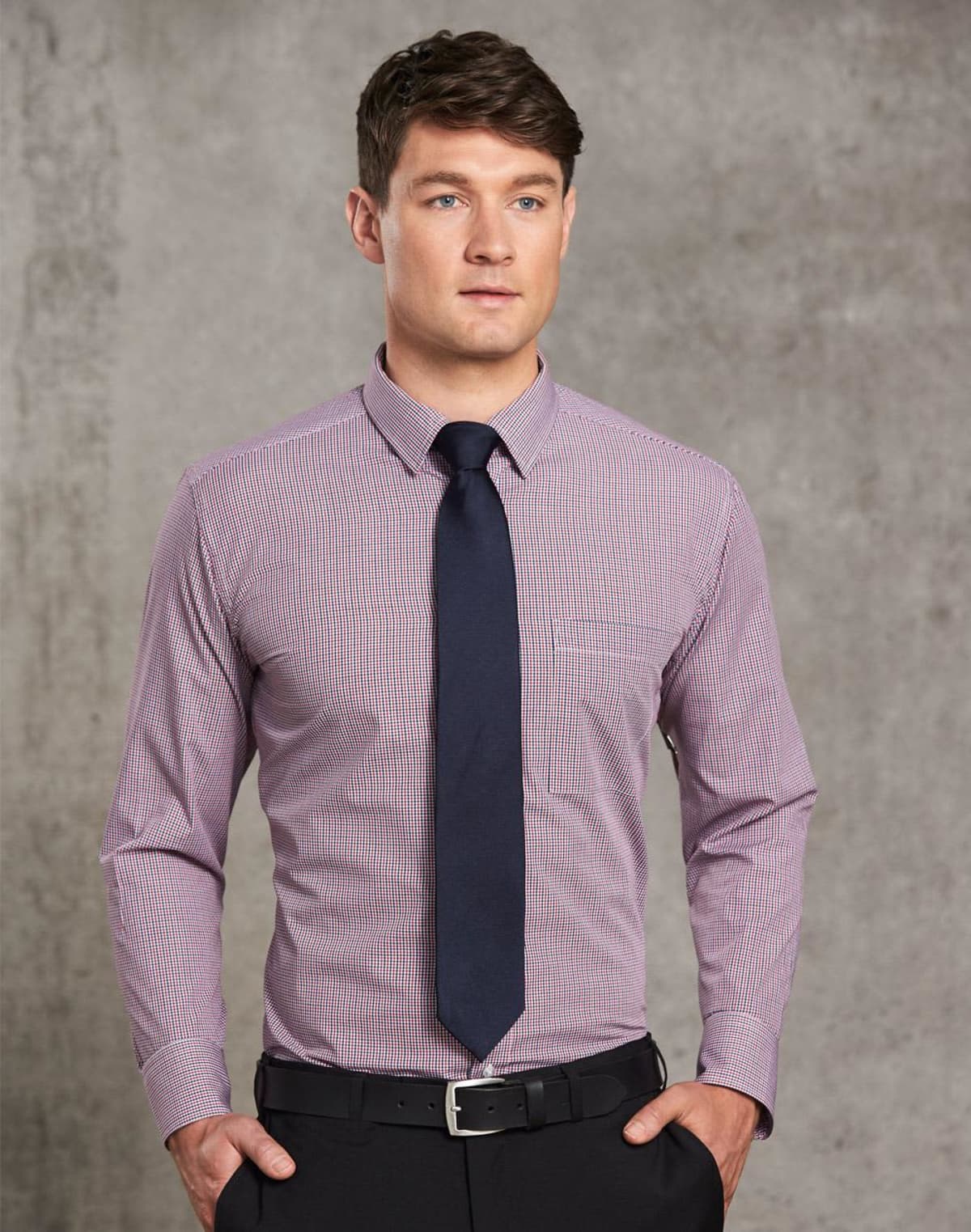 Man in a dress shirt and tie standing against a gray textured background.