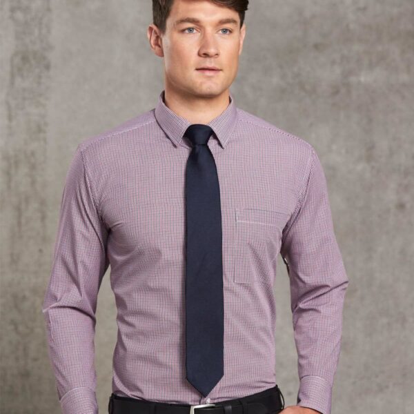 Man in a checked shirt and dark tie standing against a gray textured background.