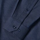 Close-up of a dark blue dress shirt sleeve with white polka dots and buttoned cuff.
