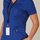 Person in blue scrubs with a blank ID badge and pen in pocket, hand on hip.