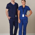 A man and woman in blue medical scrubs stand side by side, both wearing ID badges.