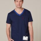 Man in navy blue medical scrubs with a name badge, standing and smiling at the camera.