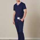 Man in navy blue scrubs stands smiling, with an ID badge clipped to his pocket.