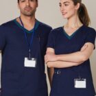 Two healthcare workers in navy blue scrubs with ID badges standing together, smiling.