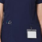 Person in navy scrubs with scissors in pocket and blank badge clipped to uniform.