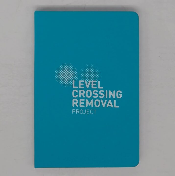 Blue notebook with Level Crossing Removal Project printed in white on the cover.