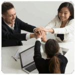 Three people in business attire stacking hands, smiling as they align on business goals.
