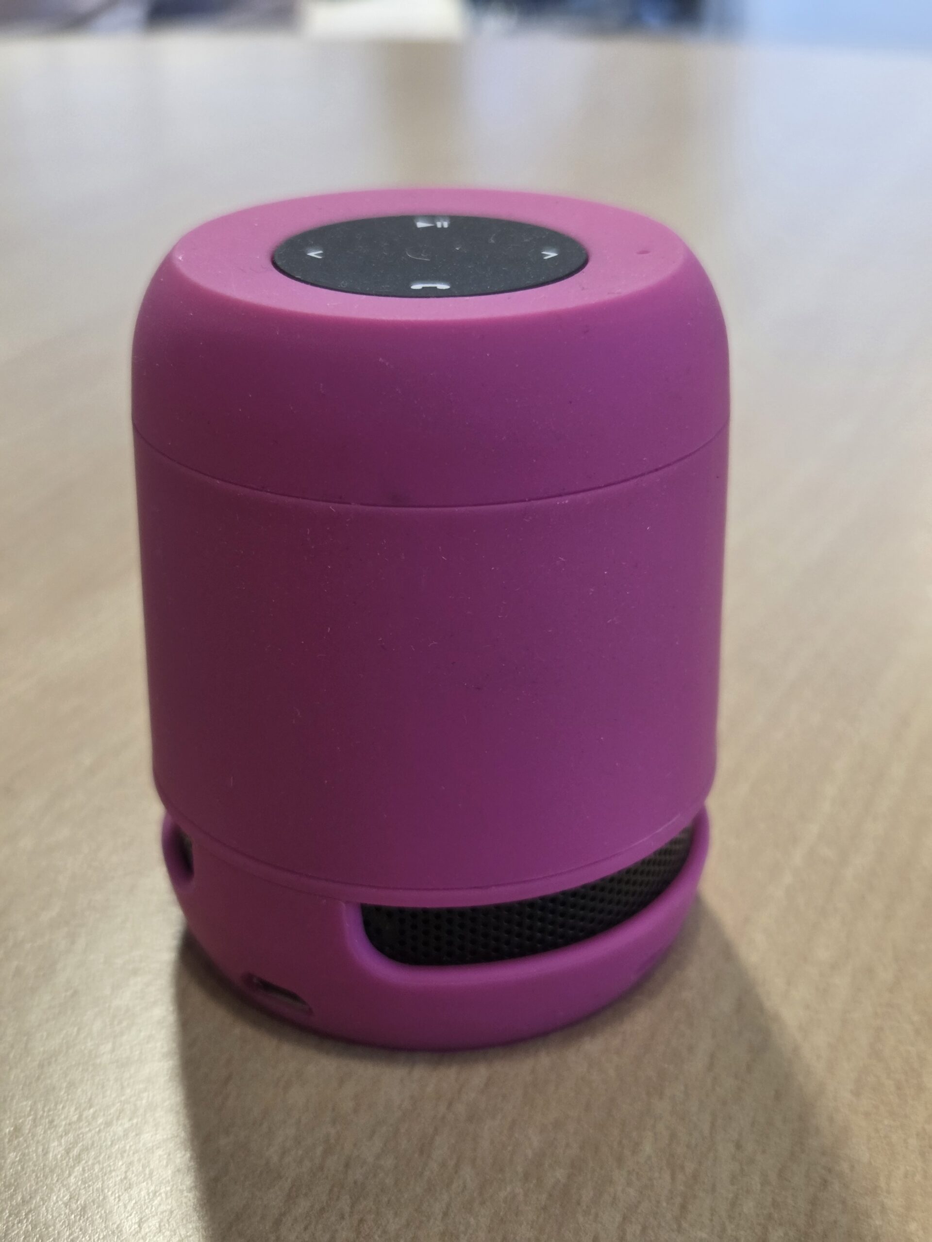 A small pink portable Bluetooth speaker, perfect as trendy merchandise, on a wooden surface.