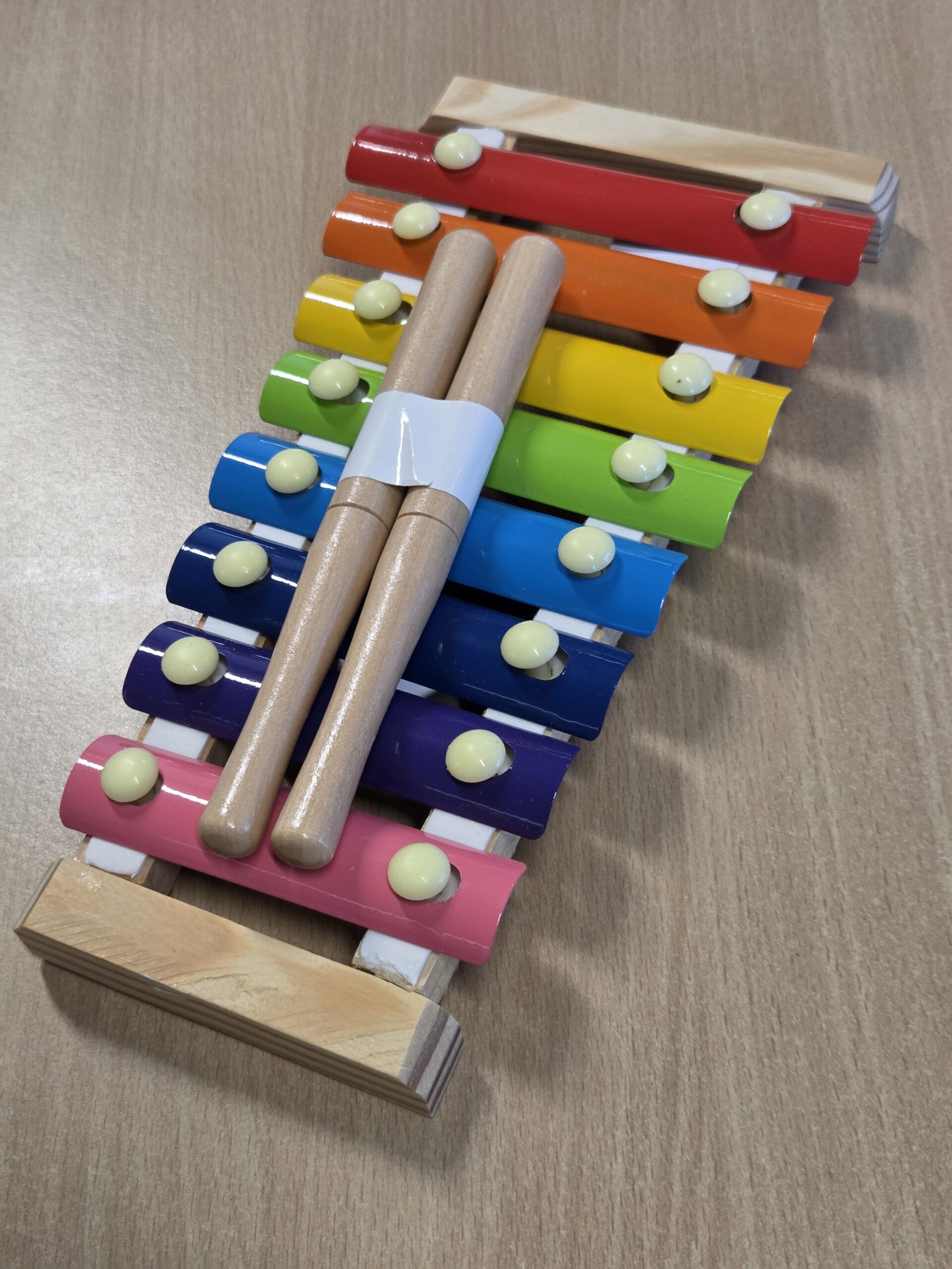 A colorful toy xylophone merchandise with two wooden mallets on a wooden surface.