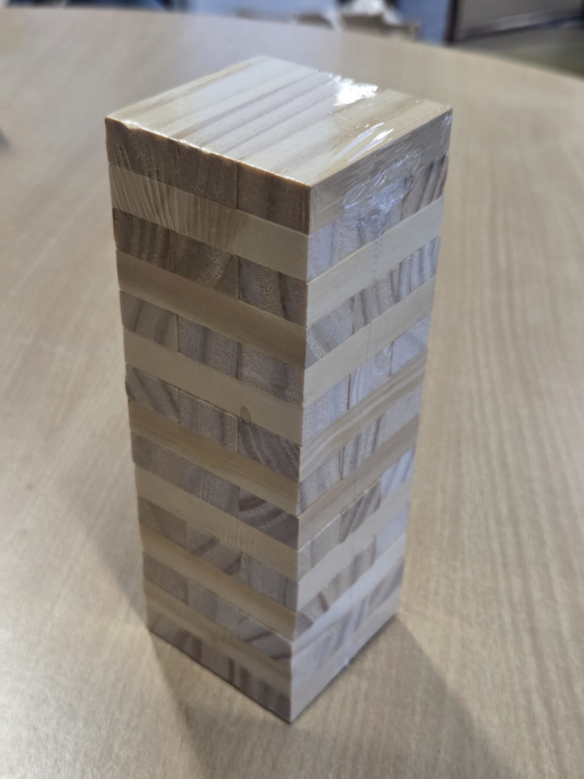 A stacked tower of wooden Jenga blocks, perfect as unique merchandise on a light wood surface.