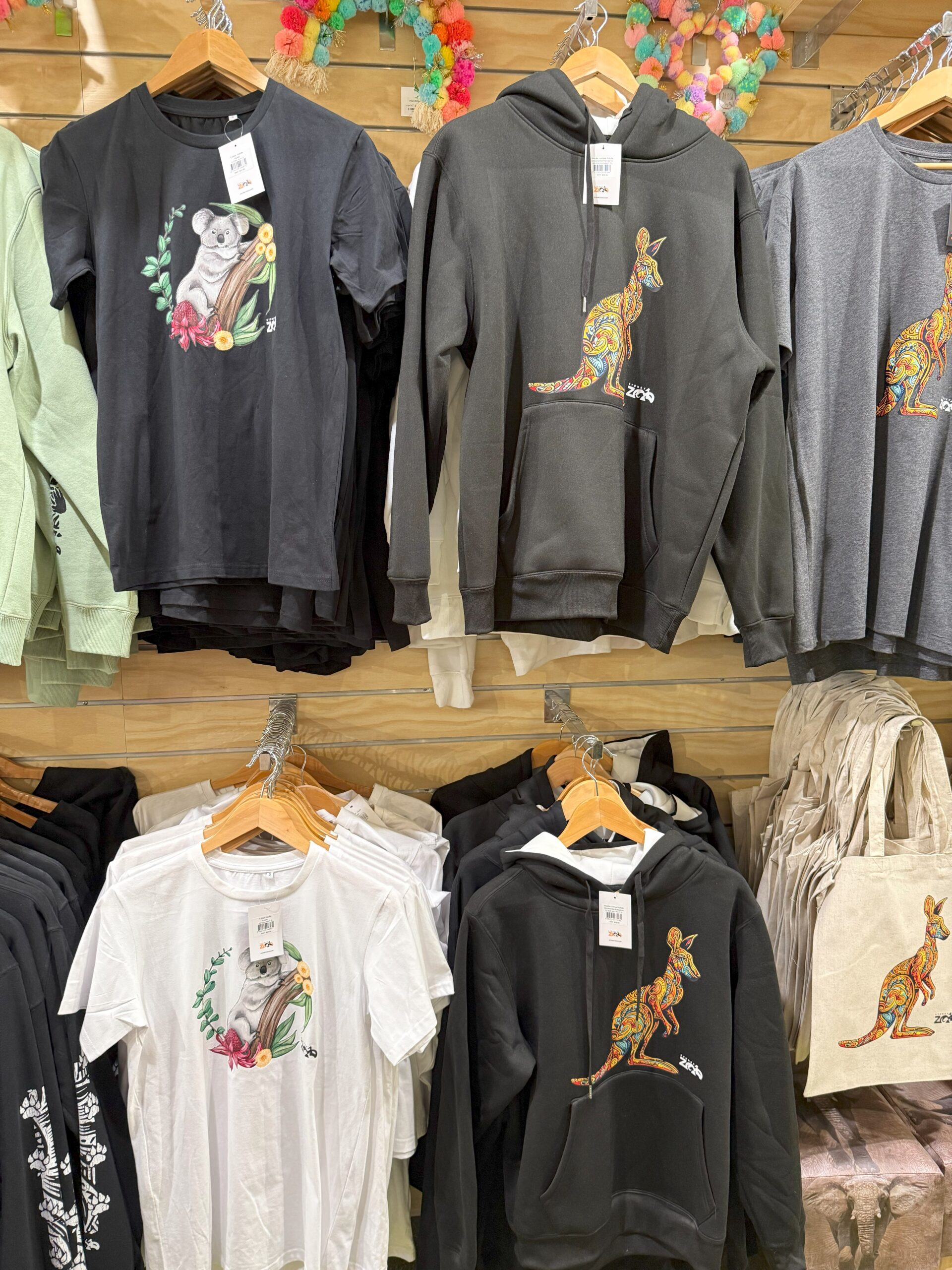 Colorful kangaroo and koala shirts—perfect zoo merchandise for experience—hang on display.