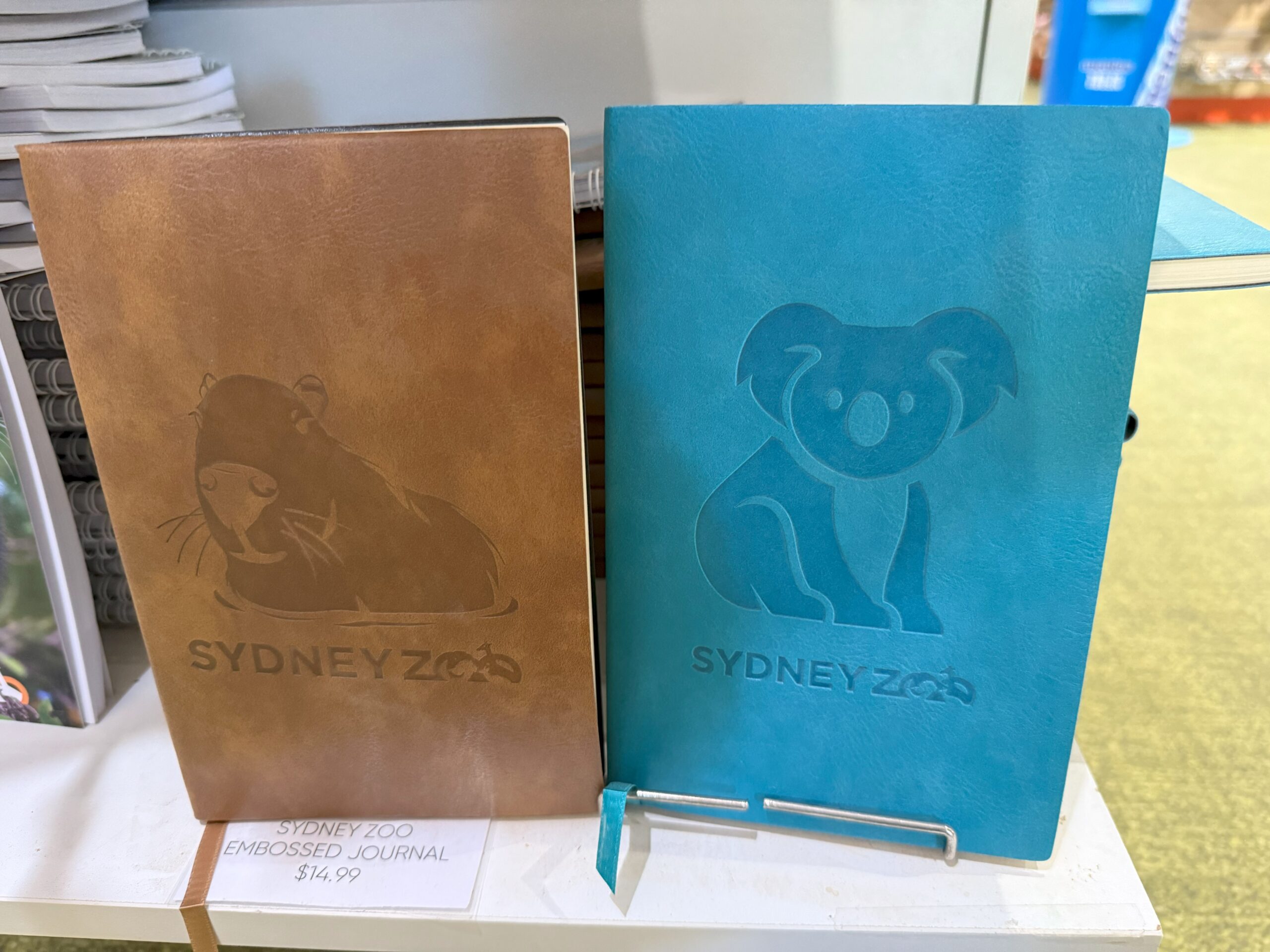 Two embossed Sydney Zoo journals: otter (brown) and koala (blue) zoo merchandise for experience.