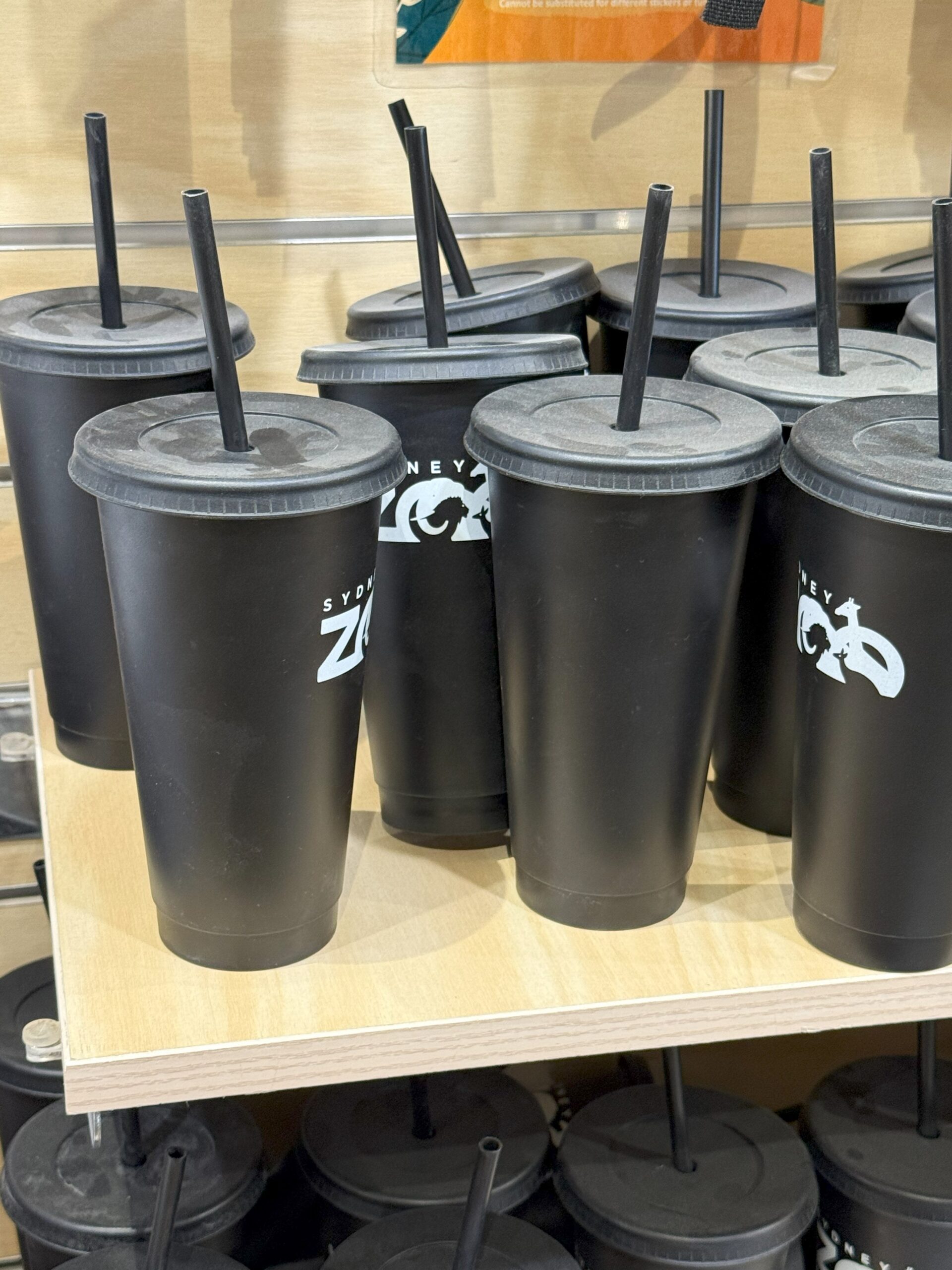 Several black reusable cups, part of zoo merchandise for experience, sit on a wooden shelf.
