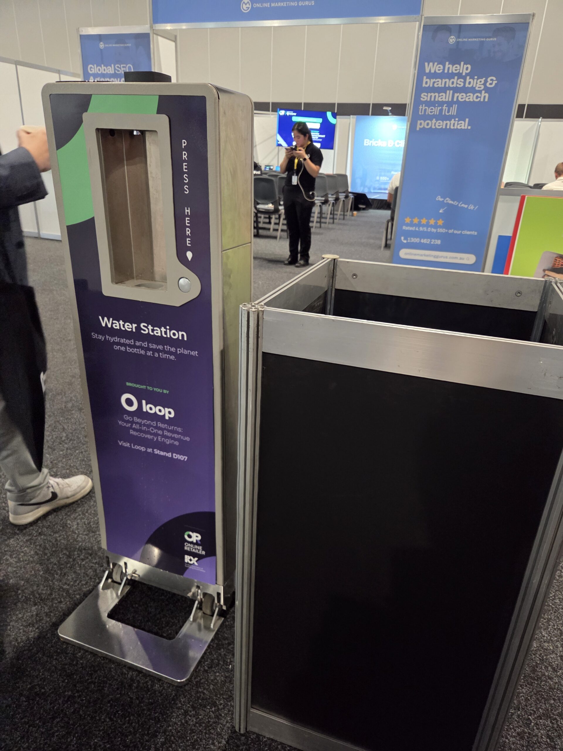 A water refill station at the Online Retailer Conference Sydney 2025, with signs in the background.