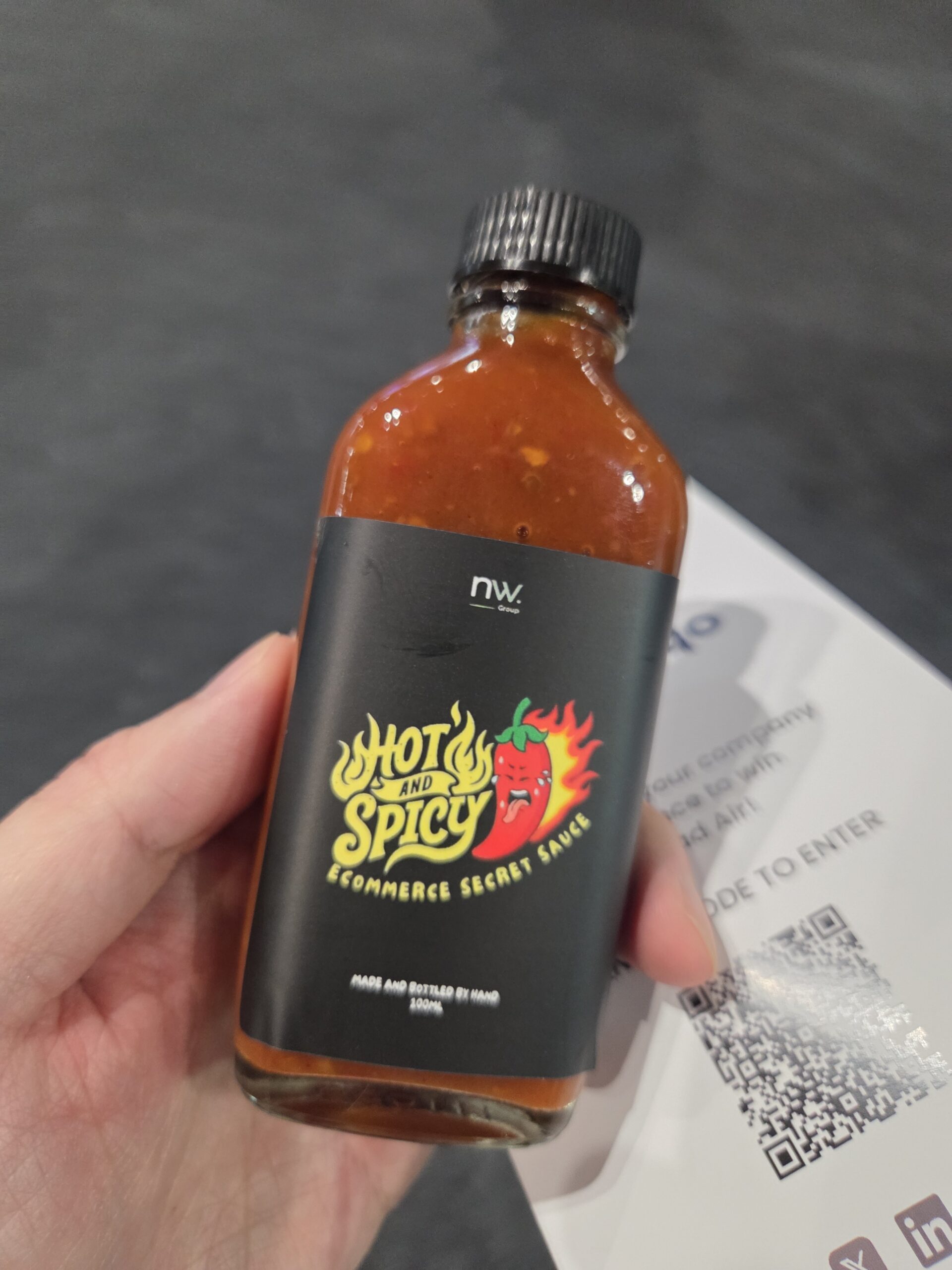 A hand holds a bottle labeled Hot and Spicy Ecommerce Secret Sauce, perfect for conference items.