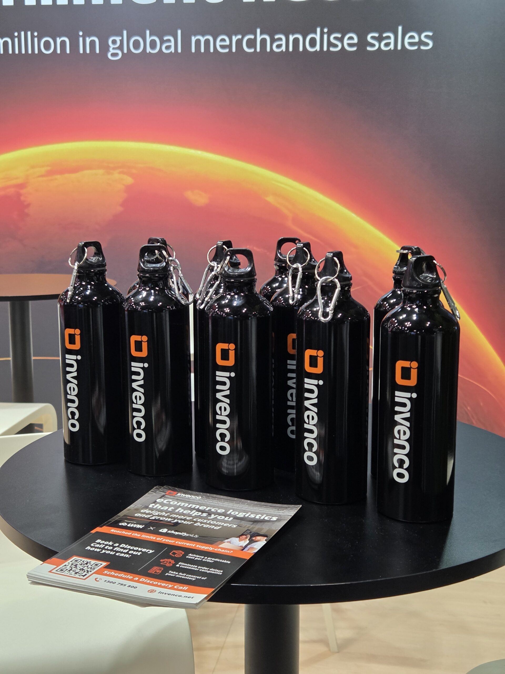 Six black Invenco water bottles, perfect conference items, on a round table with flyers in front.