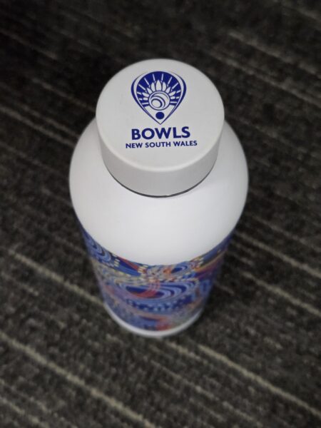 White custom bottle with Bowls New South Wales logo, placed on a dark, striped carpet.