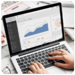 Hands typing on a laptop displaying business goals, charts, and graphs on the screen.