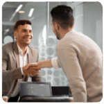Two men shaking hands in an office, smiling as they discuss business goals.