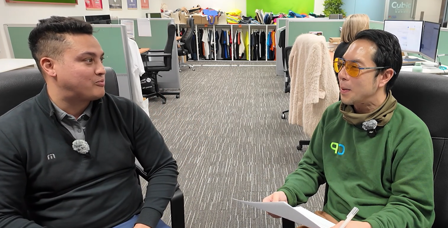 Two people discussing corporate golf in an office with desks and clothes in the background.