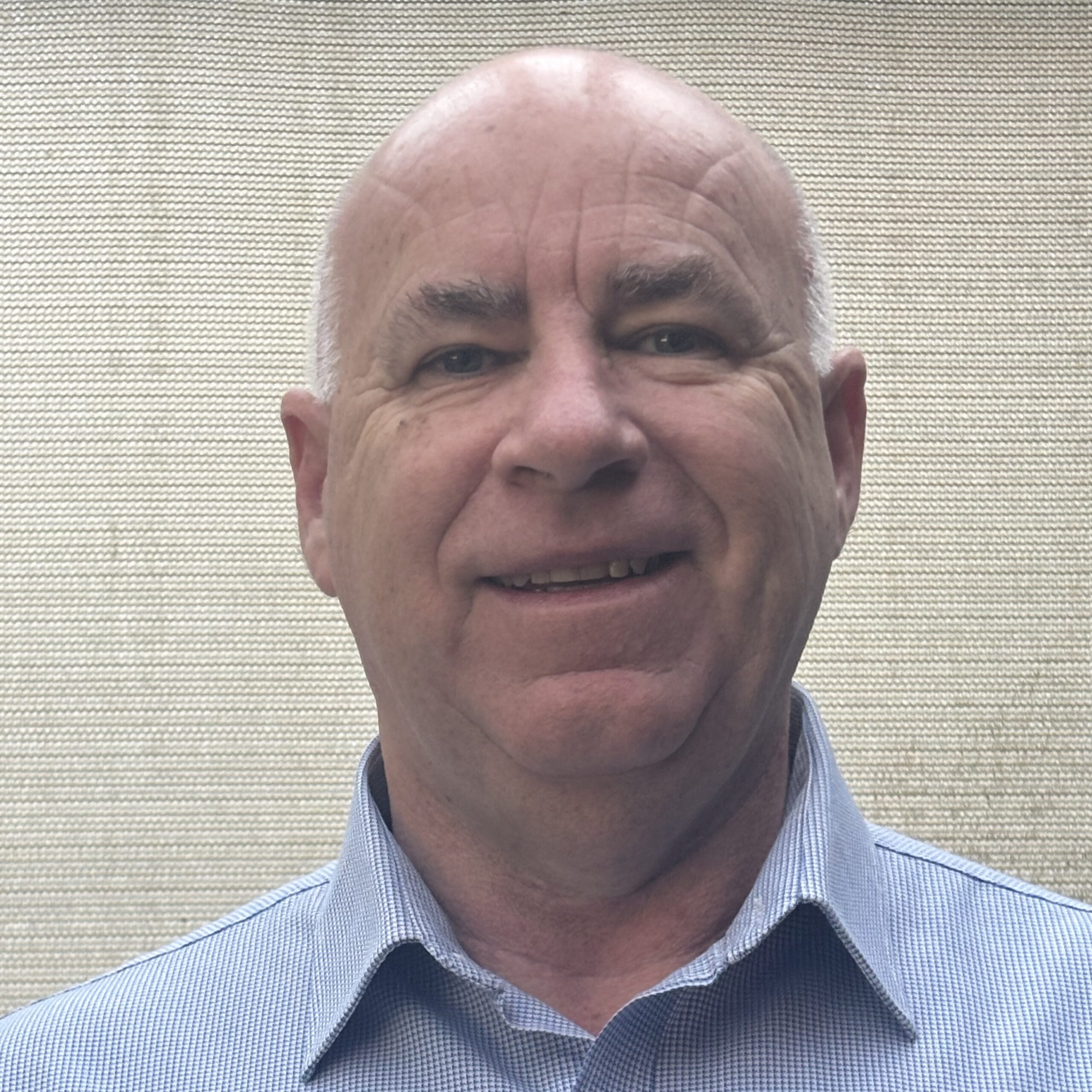 Bald man in a blue collared shirt smiling—meet the team’s friendly face.