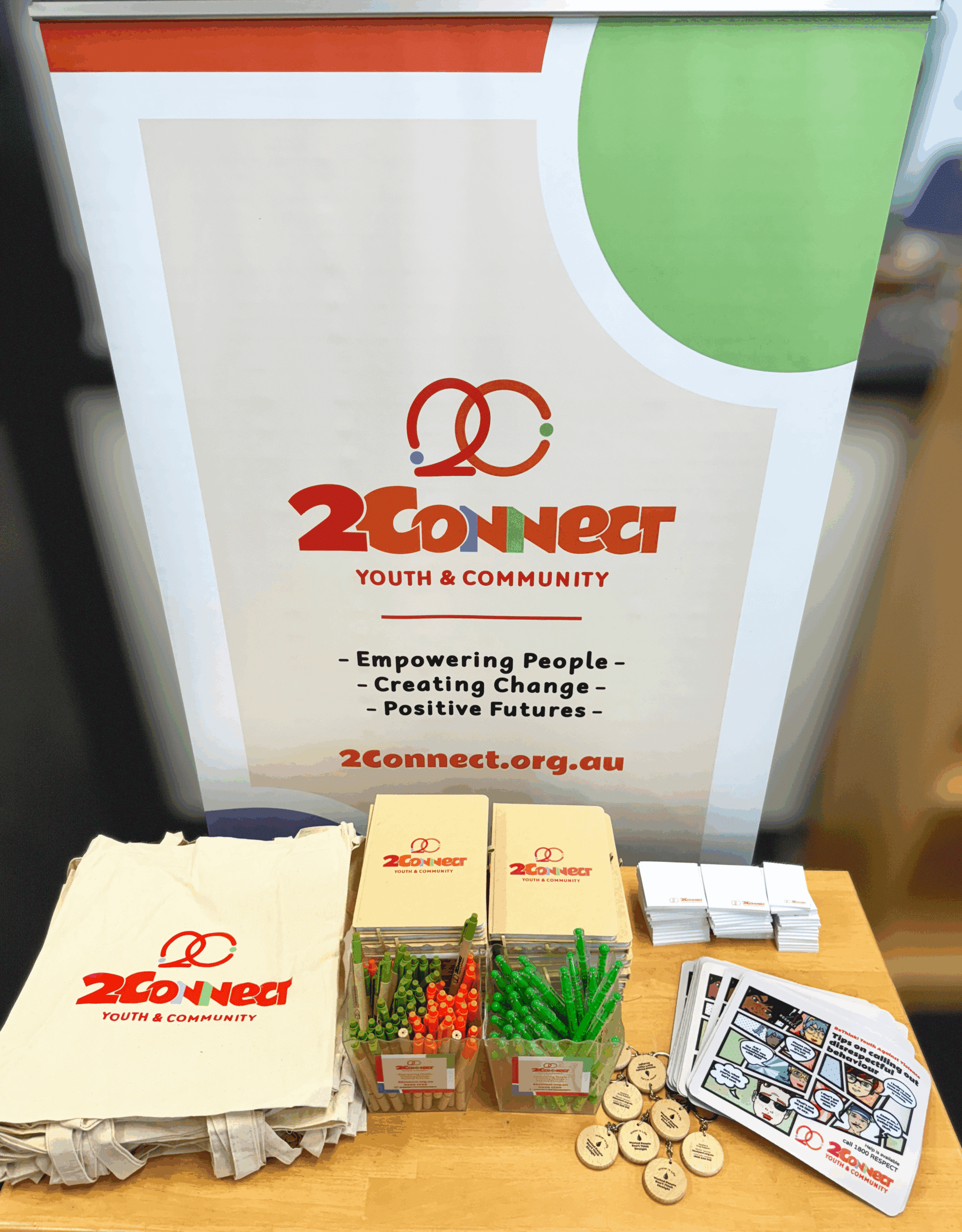 2Connect Youth & Community promo table with branded merchandise, bags, pens, badges, and flyers.