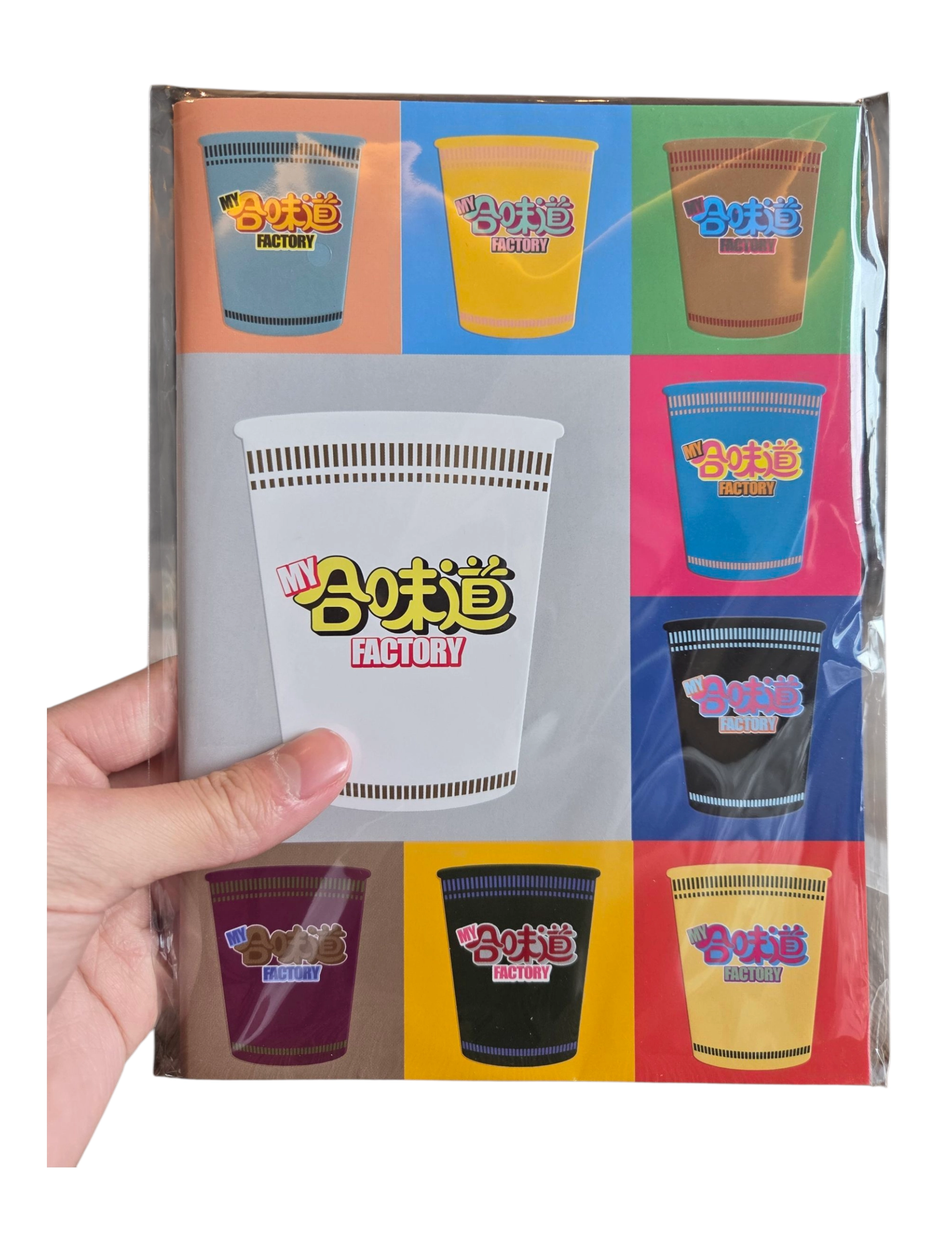 A hand holds custom merchandise: a notebook with colorful cup designs and MY 合味道 FACTORY on the cover.