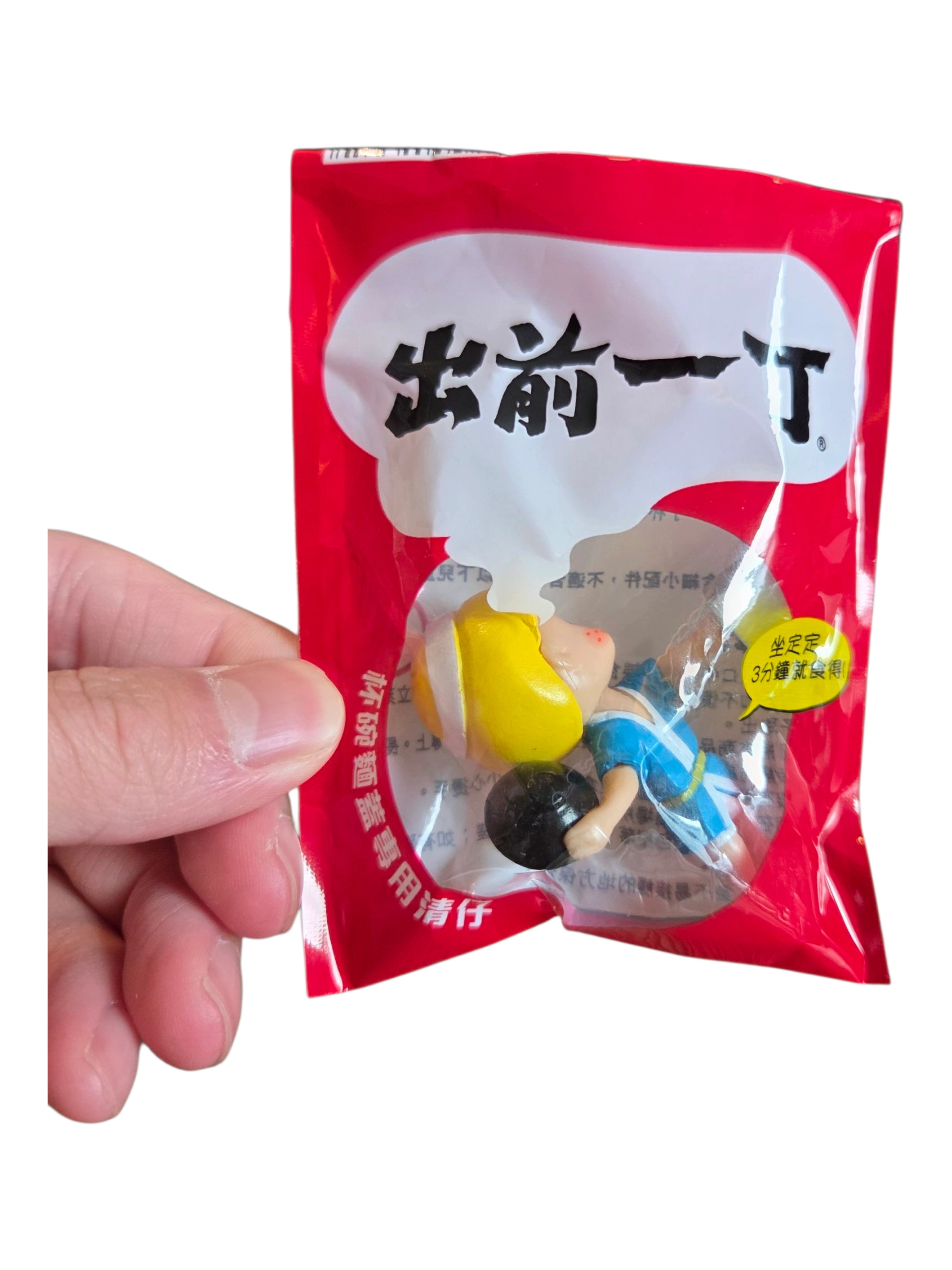 Hand holding red packet with Japanese text, custom merchandise, and a small toy figure inside.