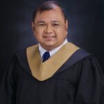 Meet the team: Smiling man in graduation gown with gold stole against a dark background.
