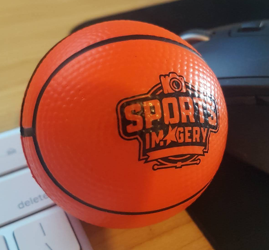 An orange mini basketball labeled Sports Imagery on a keyboard and next to a mouse.