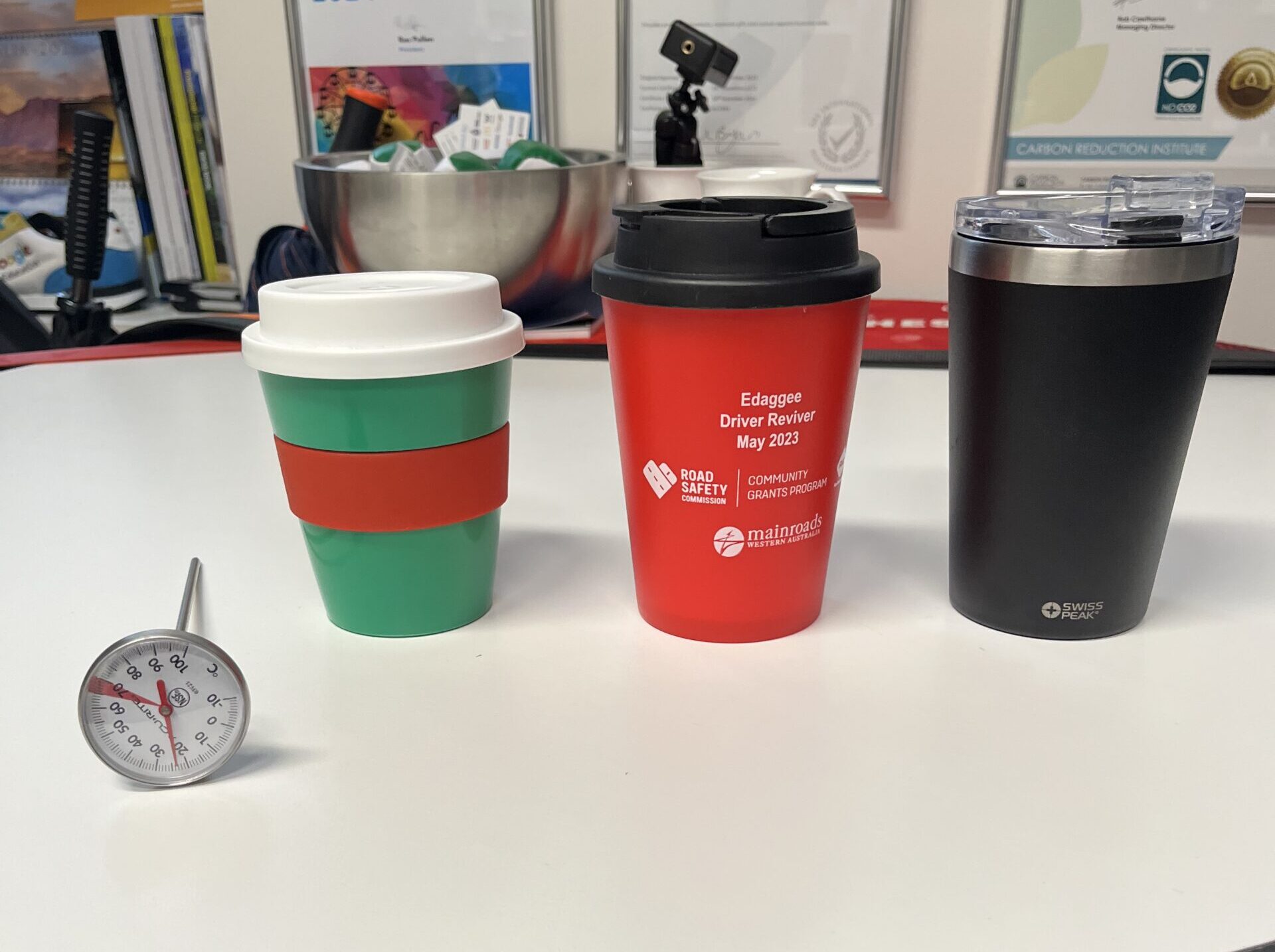 Three thermal cups and a kitchen thermometer rest on a white round table