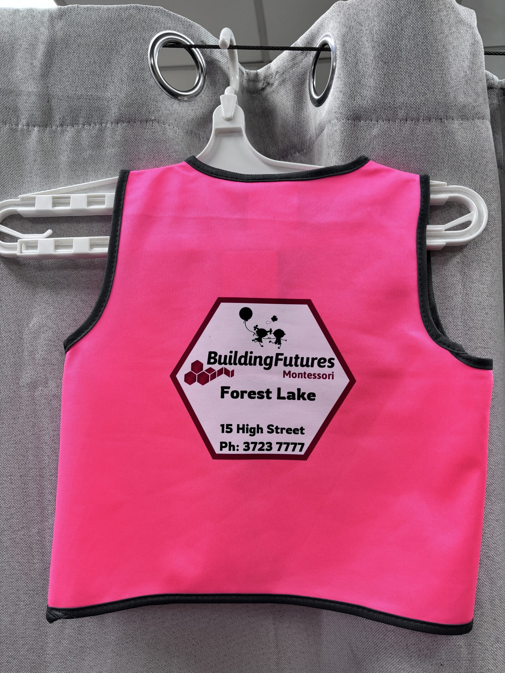 Bright pink safety vest with Building Futures Montessori Forest Lake and contact details printed.