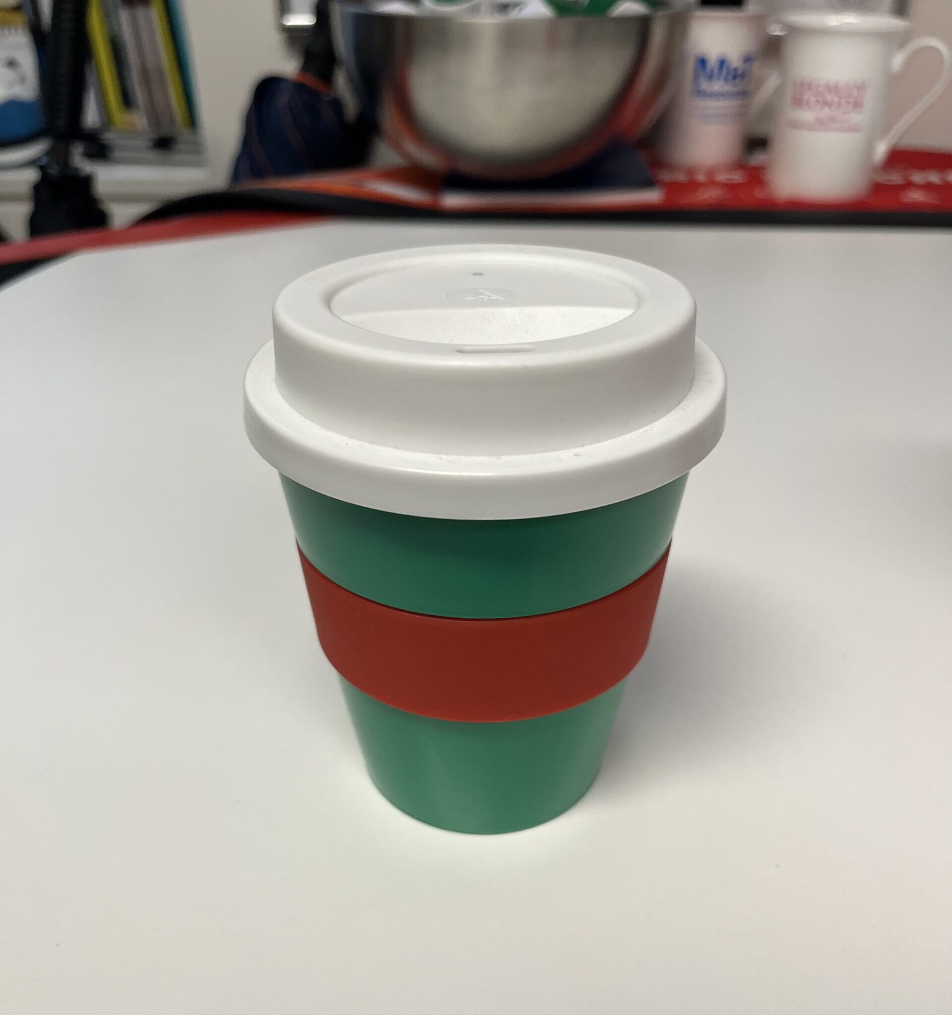 A green thermal cup with a red band and white lid