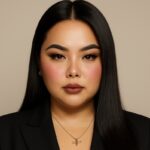 Katrina Salenga Woman with long black hair, black blazer, necklace, and pens with accessories on beige background.