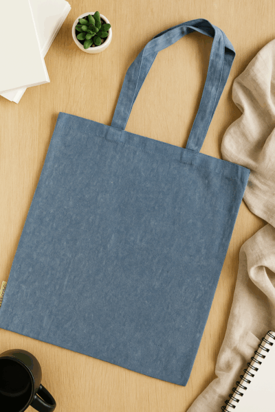 A blue denim tote bag, ideal merchandise for B2B events, on a table with books and a mug.