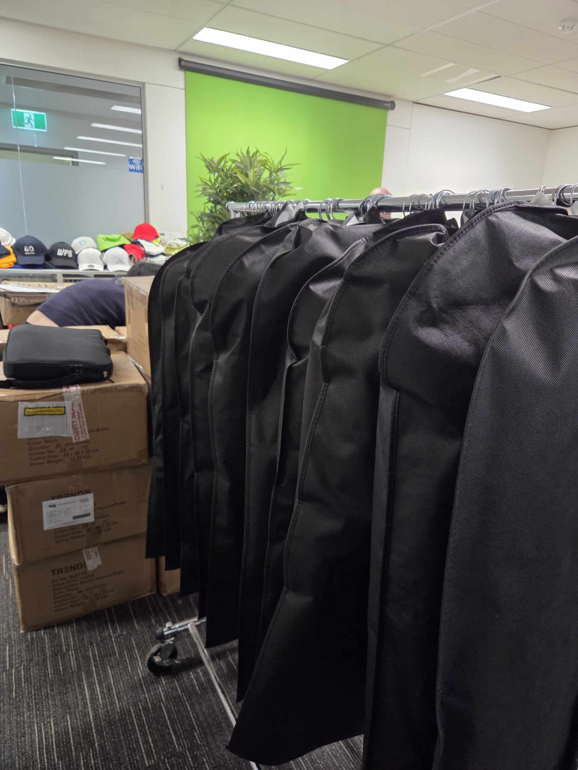 Garment bags, boxes, and hats in an office with a green backdrop at the Australasian Gaming Expo.