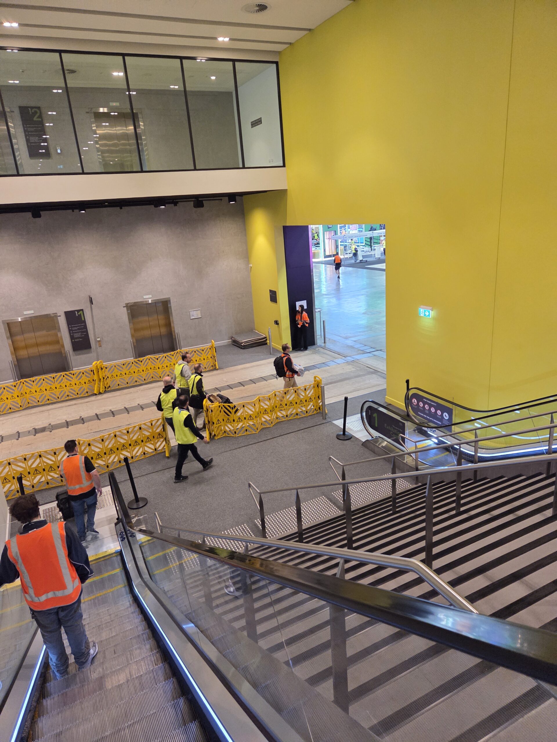 Construction workers in safety vests near elevators at the Australasian Gaming Expo.